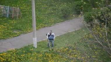 Yaşlı bir adam bahçede bir benzin makası biçiyor.