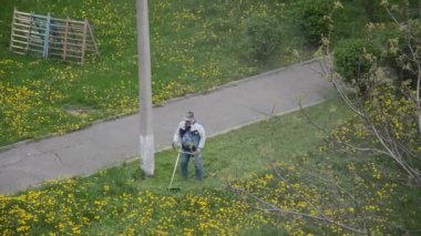 Yaşlı bir adam bahçede bir benzin makası biçiyor.