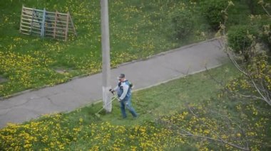 Yaşlı bir adam bahçede bir benzin makası biçiyor.