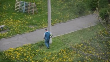 Yaşlı bir adam bahçede bir benzin makası biçiyor.