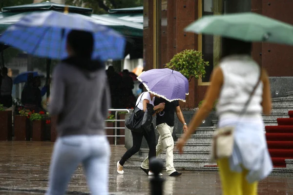 Persone che camminano con gli ombrelloni nella città piovosa — Foto Stock