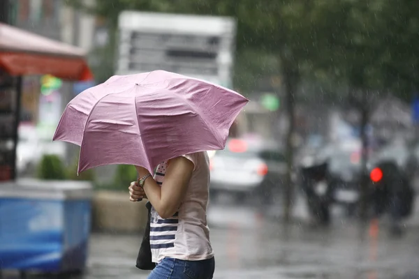 Frau läuft mit Regenschirm durch die verregnete Stadt Stockbild