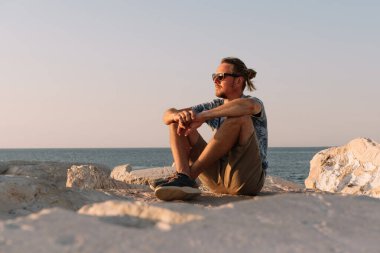 Sarışın adam yaz gündoğumunda deniz kenarında dinleniyor..