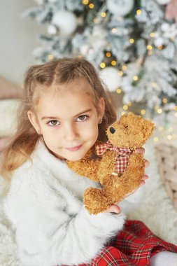 Noel ağacının arka planında oyuncak ayıyla Noel çocuğu