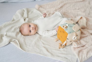 Yeni doğmuş bebek yalan söyler ve eğitici oyuncaklarla oynar. Anneliğin ve babalığın kutlu olsun. Doğum hastanesi ve kliniği. Babalar günü. Erken çocukluk gelişimi.