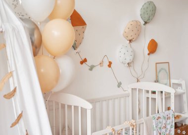 İskandinav tarzı beyaz iç mekan çocuk odası, yatak odası, çocuk odası. Kanopili bebek karyolası. Ahşap raflar ve oyuncaklar. Tente çadırı, tekstil uçurtması ve balonlar