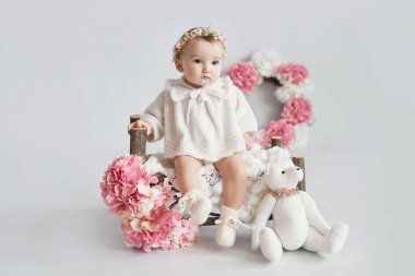 Oyuncak ayıyla örgü örüp çelenk takan tatlı bir kız. Çiçekli bahar arkaplanı. Çocuk Koruma Günü. Anneler günü tebrik kartı. Uluslararası mutluluk günü.