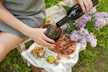 Bahçede yaz pikniği. Şarap, turta, meyve ve çiçekler. Durgun hayat. Paskalya yemeği ve masa. Bir kadının elleri şarap bardağını dolduruyor..