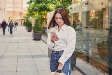 Genç ve güzel bir kadın şehirde yürüyor. Sokaktaki kızın portresi. Telefonlu eller. Çevrimiçi iş, uzaklık öğrenimi