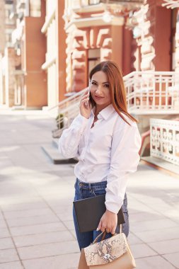 Genç ve güzel bir kadın şehirde yürüyor. Sokakta elinde telefon ve tabletle dolaşan bir kızın portresi. Paket almak ve alışveriş yapmak. Genç ve güzel bir kadın şehirde yürüyor. Çevrimiçi iş, uzaklık öğrenimi