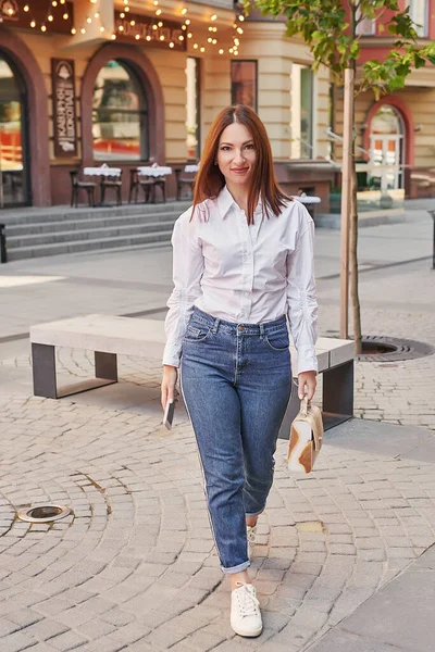 Genç ve güzel bir kadın şehirde yürüyor. Sokaktaki kızın portresi. Telefonlu eller. Çevrimiçi iş, uzaklık öğrenimi