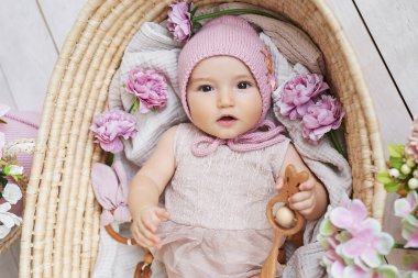 Hasır sepetin içinde çıngıraklı çiçek şapkalı küçük kız. Anneler Günü ve Paskalya kartı. Çocuk Koruma Günü. Dünya Mutluluk Günü. Gülümseyen çocuk