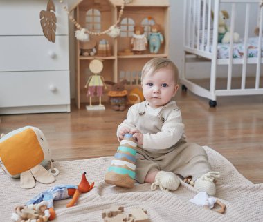 Mavi gözlü harika bir erkek bebek. Çocuk, çocuk odasında oyuncaklarla oynuyor. Erken gelişim, anaokulu, kreş, oyun odası. Çocuk Günü, Anneler Günü.