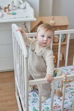 Beşikte mavi gözlü harika bir erkek bebek. Çocuk, çocuk odasında oyuncaklarla oynuyor. Erken gelişim, anaokulu, kreş, oyun odası. Çocuk Günü, Anneler Günü.