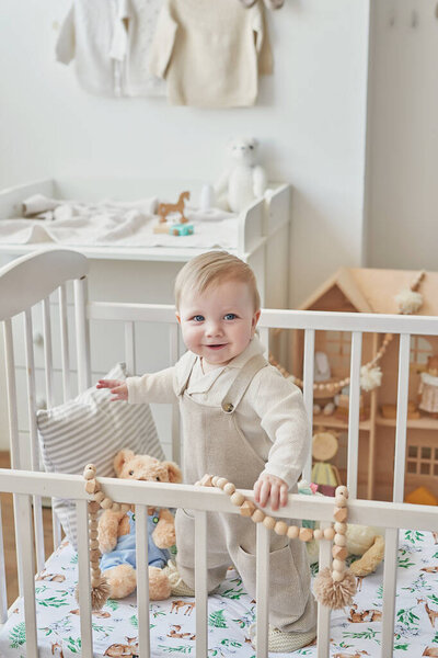 Wonderful baby boy with blue eyes in crib. Child playing with toys in nursery. Early development, kindergarten, nursery, playroom. Children's Day, Mother's Day.