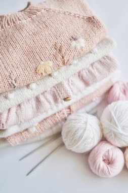 Stack of knitted clothes and balls of yarn, knitting needles, accessories for knitting. Baby clothes. Needlework, hobby, knitting, handwork