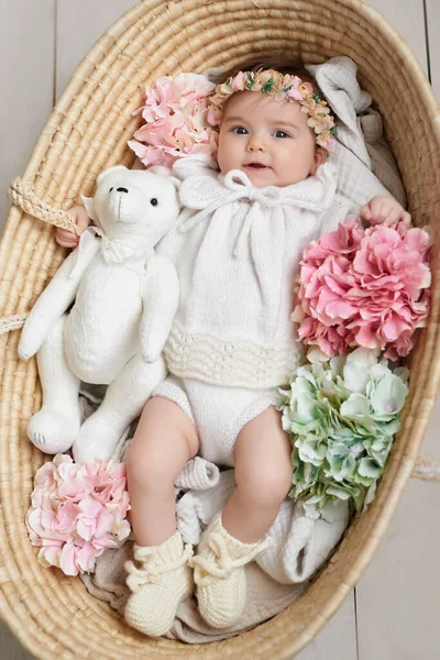 Hasır sepetin içinde çıngıraklı çiçek şapkalı küçük kız. Anneler Günü ve Paskalya kartı. Çocuk Koruma Günü. Dünya Mutluluk Günü. Gülümseyen çocuk