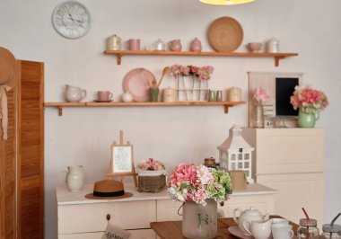 White kitchen interior in loft style. Shelves with pink crockery and kitchen utensils. Studio apartment. Rent and delivery of housing. Hostel and hotel.