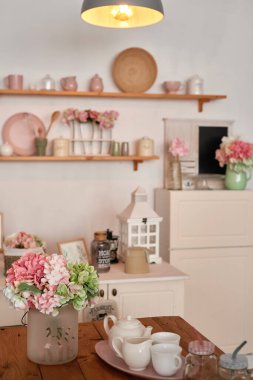 White kitchen interior in loft style. Shelves with pink crockery and kitchen utensils. Studio apartment. Rent and delivery of housing. Hostel and hotel.