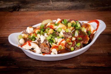 Ördek konfeti poutine tabağı ahşap masa poutine, patates kızartması ve peynir püresi ile yapılan bir Kanada yemeğidir.