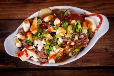 Ördek konfeti poutine tabağı ahşap masa poutine, patates kızartması ve peynir püresi ile yapılan bir Kanada yemeğidir.