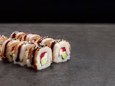 İçinde avokado ve krem peynir olan Japon Unagi suşi rulosu. Üzerinde sos ve koyu beton arkaplan olan yılan balığı parçaları. Uzay resmini kopyala. Tek bir nesne. Suşinin içi dışına çıktı.