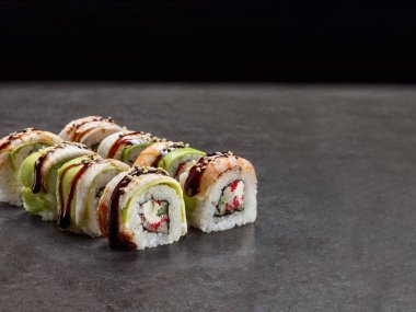 İçinde salatalık ve krem peynir olan Japon suşi rulosu. Üzerinde karides, karides, avokado ve beton arkaplanda sos olan Asya yemekleri. Tek bir nesne. Suşinin içi dışına çıktı.