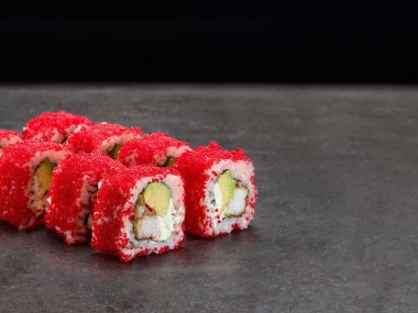Japon suşisinin içinde çıtır kara kaplan karidesi ve içinde avokado ve krem peynir var. Kırmızı uçan balık yumurtası Tobiko üstte. Masago havyarlı Asya böreği. İçi dışına çıkmış suşi. Somut arkaplan.