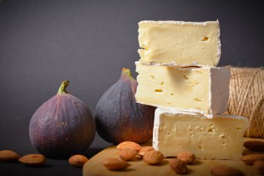 Krem peynirli krem peynirin yan görüntüsü. Yumuşak peynirli peynir tahtası. Tahta arka planda badem fıstığı ve incir meyveleriyle servis edilen tabaklar. Beyaz yumuşak peynir. Aperatifler ve başlangıçlar.