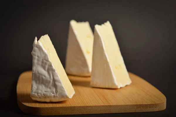 在黑色背景的木板上紧密贴上柔软的法式Brie奶酪片 三块奶酪做的一盘奶酪 — 图库照片