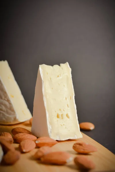 用柔软的法国布里奶酪片与杏仁坚果一起放在深色背景的木板上的芝士板的关闭 三块芝士和杏仁开胃菜开胃菜小吃垂直图像 — 图库照片