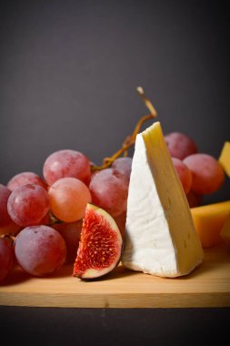 Peynir tahtasını yumuşak peynir parçaları, kırmızı üzümler ve incir kesikleriyle kapatın. Siyah arka planda bir tabak. Beyaz küflü Fransız peyniri. Yatay görüntü. Aperatifler ve başlangıçlar