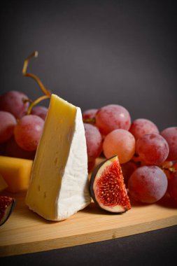 Yumuşak peynirli, pembe üzümlü ve incirli leziz bir peynir tahtası. Siyah arka planda meyve kesimi ve üzümlü beyaz küflü Fransız peyniri. Dikey boşluk resmi