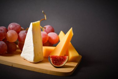 Sert ve yumuşak Fransız peyniri, pembe üzümler ve incir dilimleriyle lezzetli sağlıklı peynirin yan görüntüsü. Beyaz küflü peynir, meyve dilimleri ve siyah arka planda üzüm. Boşluk resmini kopyala