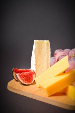 Sert ve yumuşak peynirli lezzetli peynir tahtası, pembe üzümler ve incir dilimleriyle kapatın. Siyah arka planda meyve kesimi ve üzümlü beyaz küflü Fransız peyniri. Dikey boşluk resmi