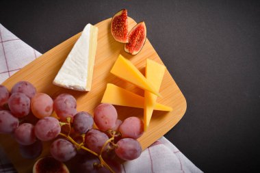 Lezzetli, sağlıklı peynirli, sert ve yumuşak peynirli, pembe üzümlü ve incirli peynirin tam üstünde. Meyve dilimleri ve üzümlü beyaz küflü Fransız peyniri, siyah arka planda mutfak havlusu.