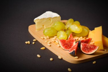 Siyah arka planda çam fıstığı ile servis edilen peynirin yan görünüşü. Yeşil üzüm ve incir dilimli sert ve yumuşak Fransız peyniri parçaları. Tabakta beyaz küflü peynir. Tahtada aperatifler.