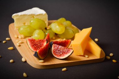 Siyah arka planda çam fıstığı servis edilir. Ön planda yeşil üzüm ve incir kesikli sert ve yumuşak Fransız peyniri parçaları. Tabakta beyaz küflü peynir. Tahtada aperatifler.