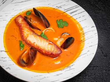 Siyah beton arka planda beyaz tabakta servis edilen somon balığı çorbası. Somon, midye, karides, karides, mürekkep balığı ve sebzeli sıcak Bouillabaisse çorbası. Geleneksel Fransız yemeği. Restoran menüsü