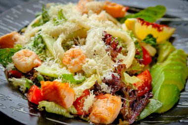 Baharatlı deniz ürünleri salatası ızgara somon, karides, kalamar, avokado, vişneli domates, parmesan peynirli marul. Siyah tabakta sıcak salata yakın. Restoran menüsü