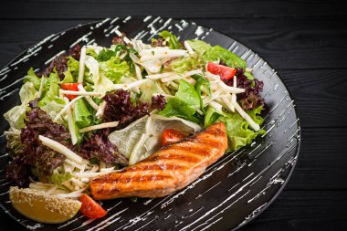 Izgara somonlu taze salata. Kereviz, elma, limon, marul ve vişneli domatesli kızarmış somon, ahşap zemin üzerinde servis edilir. Norveç Lokantası menüsü.