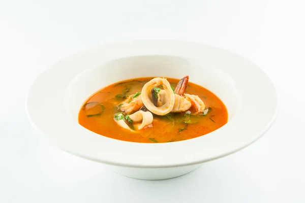 French seafood soup with white fish fillet, mussels, shrimp, squid, fresh basil and leek. Traditional soup with rockfish and mussel served in white plate. First dish isolated on white background
