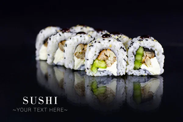 Unagi Japon suşisini ters yüz edip salatalık ve yılan balığıyla sarın. Susam tohumlarıyla servis edilir. Siyah arka planda yansımalı Asya yemeği. Metin Alanı olan Pankart