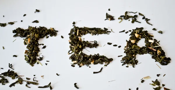 Das Wort "Tee" gestapelt mit grünem Teeblatt auf einer weißen Untertasse auf weißem Hintergrund — Stockfoto