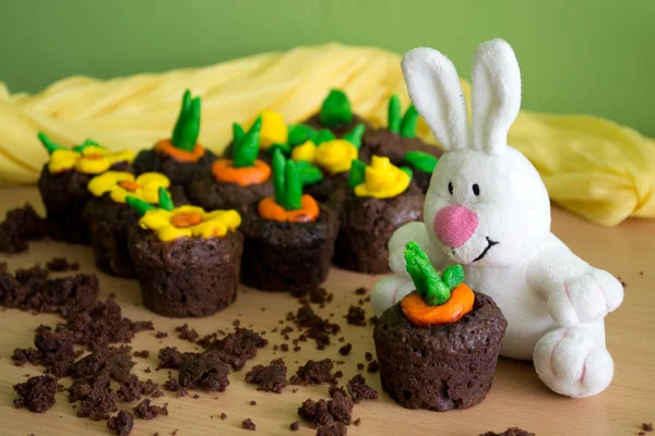 Chocolate muffins with fondant decorations in the shape of flowers and vegetables in spring brilliant colors and white plush rabbit