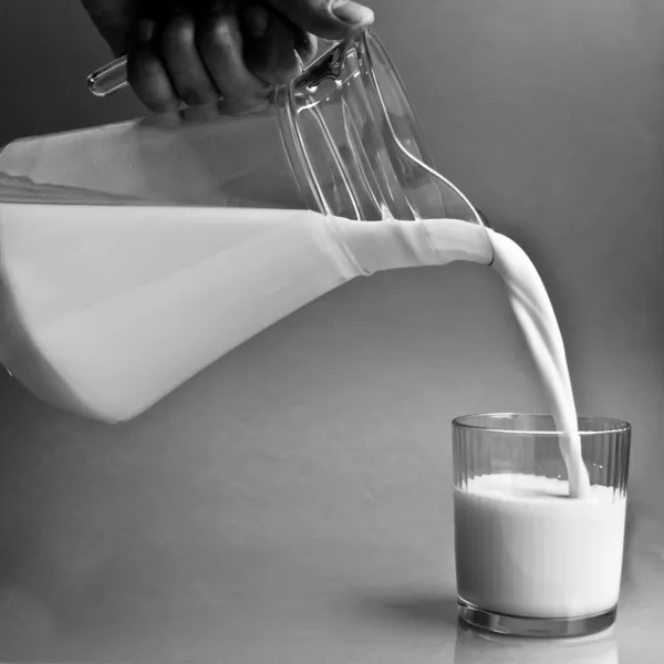 Milch aus einem Krug in ein Glas gießen — Stockfoto