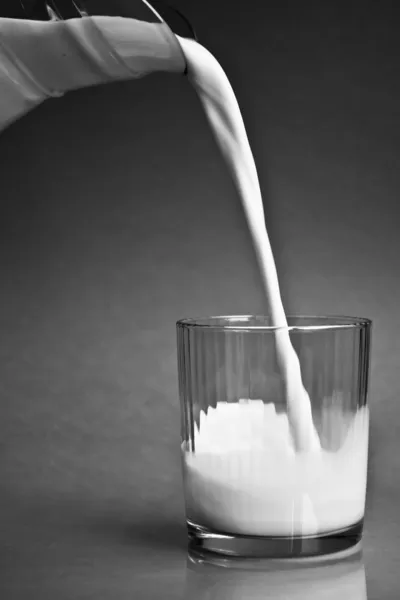 Milch aus einem Krug in ein Glas gießen Stockbild