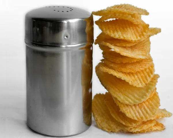 Stapel welliger Chips neben Salzstreuern aus Stahl auf weißem Hintergrund lizenzfreie Stockfotos
