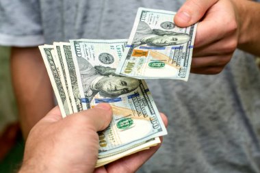 Bir kişi, bir diğerinin yanından yüz dolarlık banknotlar geçirir.