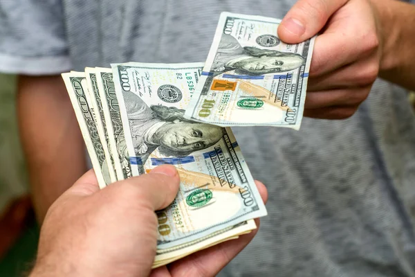 Bir kişi, bir diğerinin yanından yüz dolarlık banknotlar geçirir.